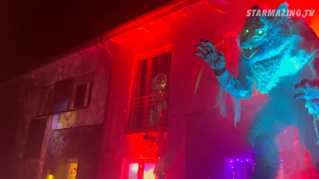 Vorgarten Halloween in Mönchengladbach: 3 Meter großer Werwolf und Kürbiskönig im Fenster 3 Meter großer Werwolf steht im Vordergrund beim Vorgarten Halloween in Mönchengladbach Rheydt, während der Kürbiskönig im Fenster auf seinem Thron sitzt und gruselig beleuchtete Häuser die Szenerie abrunden.