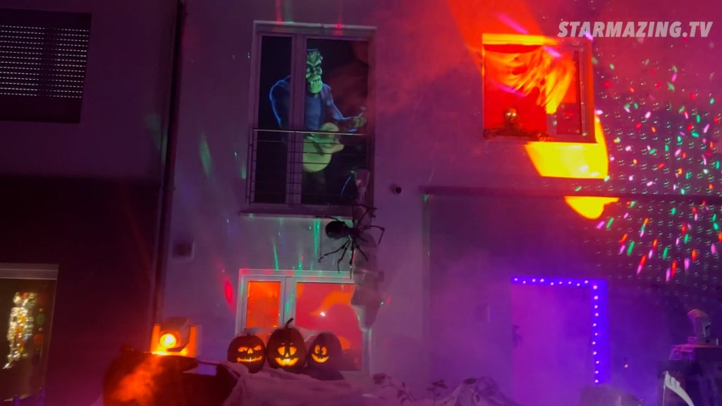 Vorgarten Halloween Rheydt: Frankenstein rockt die Gitarre neben Riesenspinne und Lichtshow Frankenstein spielt Gitarre, während eine Riesenspinne eine Person an der Hauswand eingesponnen hat, umgeben von einer leuchtenden Lichtshow beim Vorgarten Halloween Rheydt.