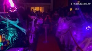 Eine Gruppe kostümierter Kinder beobachtet gespannt einen gruseligen Clown, der in einem Paketkastenkäfig beim Halloween-Event in Rheydt auszubrechen droht.